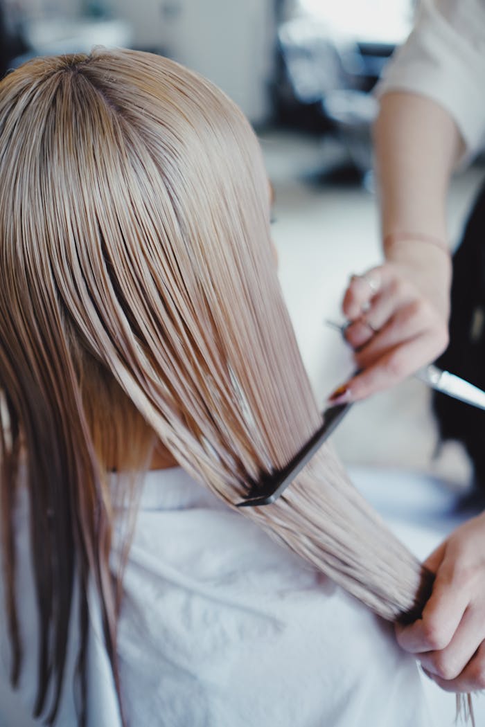 Close-up of a hairstylist arranging long, straight blonde hair in a salon environment.