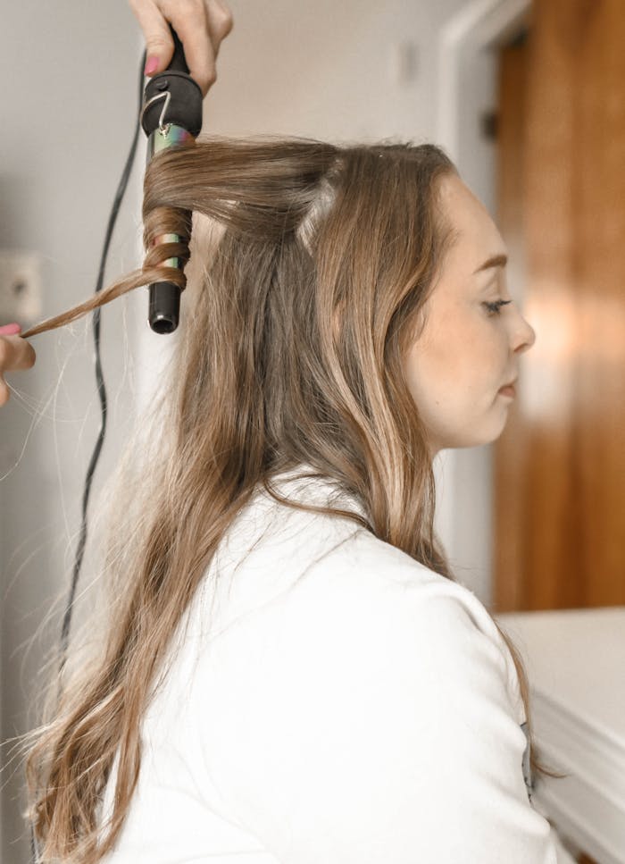 About Profile of a woman having her hair curled with an iron in a salon setting.